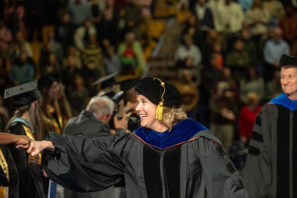 Faculty fist bumps graduate during commencement processional.